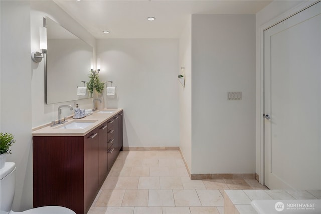 bathroom with toilet, double vanity, baseboards, and a sink