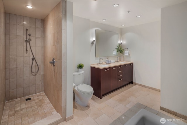 bathroom featuring double vanity, toilet, a sink, tiled shower, and baseboards