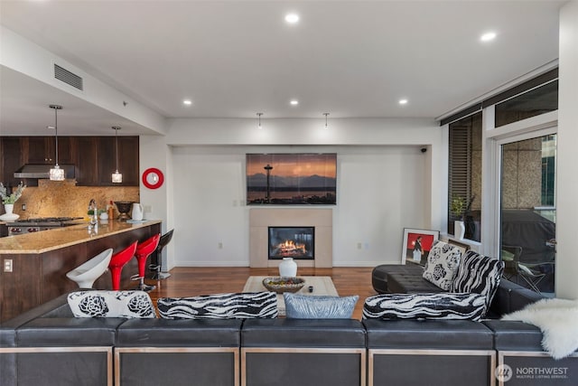 living room with a glass covered fireplace, visible vents, recessed lighting, and wood finished floors