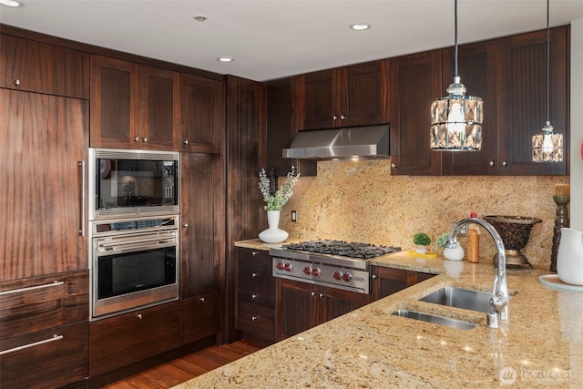 kitchen with stainless steel appliances, hanging light fixtures, decorative backsplash, a sink, and under cabinet range hood