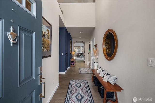 interior space with dark wood-style floors, arched walkways, a high ceiling, and baseboards