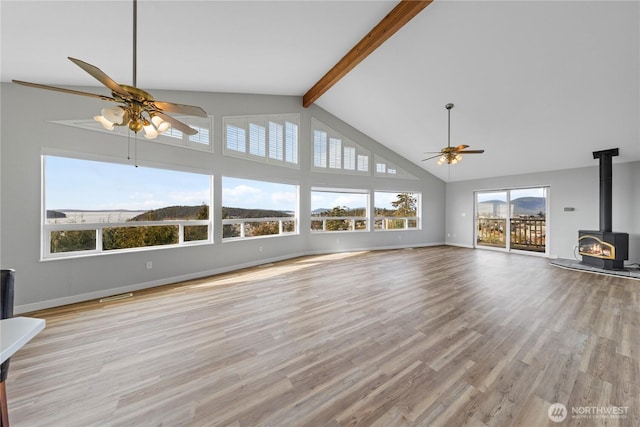 unfurnished living room with wood finished floors, a ceiling fan, baseboards, beam ceiling, and a wood stove