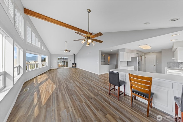 living room featuring baseboards, wood finished floors, beamed ceiling, a wood stove, and high vaulted ceiling