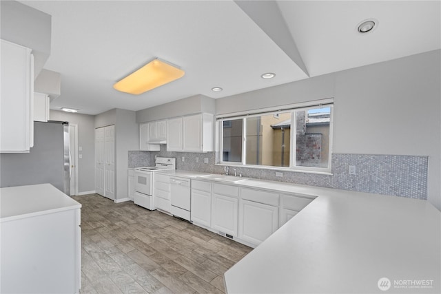 kitchen featuring light countertops, backsplash, white cabinetry, a sink, and white appliances