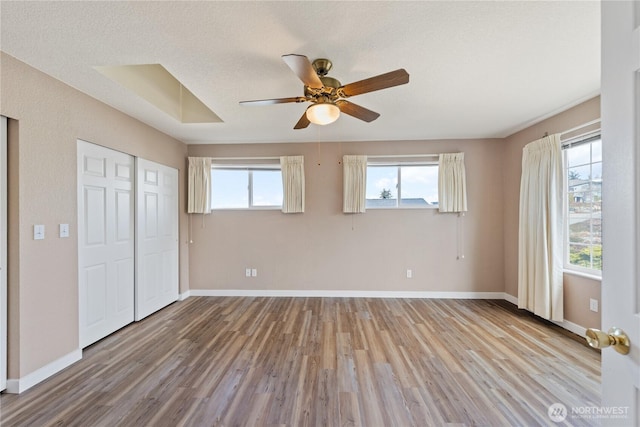 unfurnished bedroom with baseboards, multiple windows, a closet, and light wood-style floors