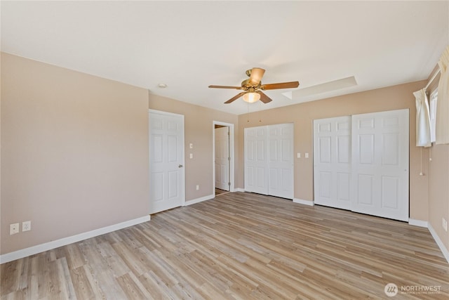 unfurnished bedroom with light wood-style floors, ceiling fan, baseboards, and multiple closets