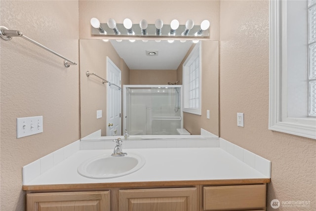 full bath with a textured wall, a shower stall, and vanity