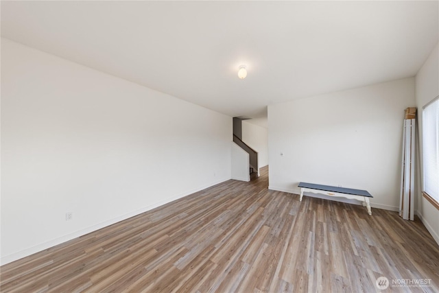 unfurnished room featuring baseboards, light wood finished floors, and stairs