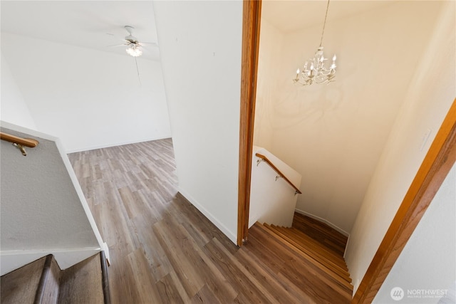 staircase featuring ceiling fan with notable chandelier, baseboards, and wood finished floors