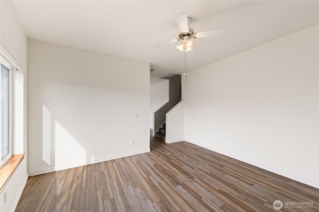 spare room with wood finished floors, ceiling fan, baseboards, and stairs