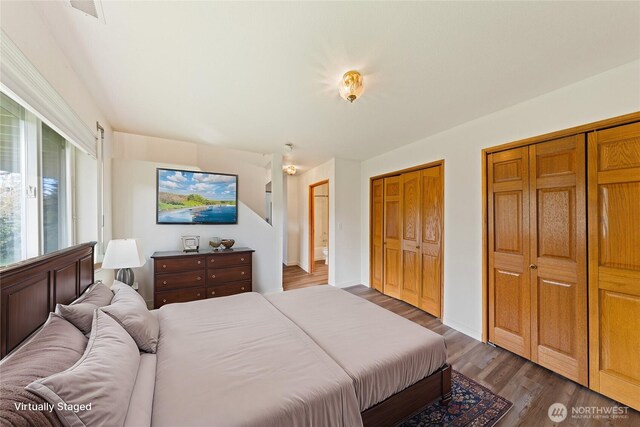 bedroom with wood finished floors, two closets, and visible vents