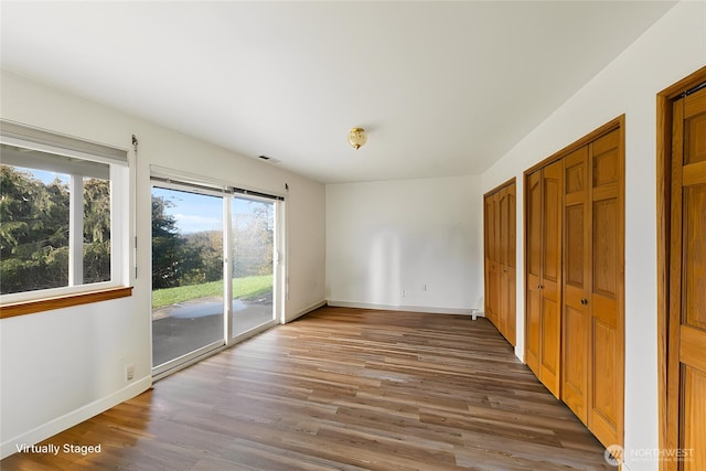 unfurnished bedroom with baseboards, wood finished floors, visible vents, and access to exterior