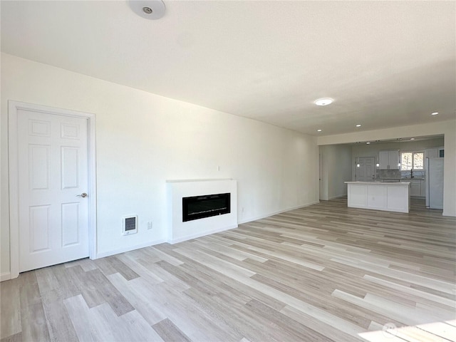 unfurnished living room with light wood finished floors, a fireplace, visible vents, and baseboards