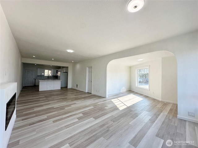 unfurnished living room featuring arched walkways, light wood finished floors, and baseboards