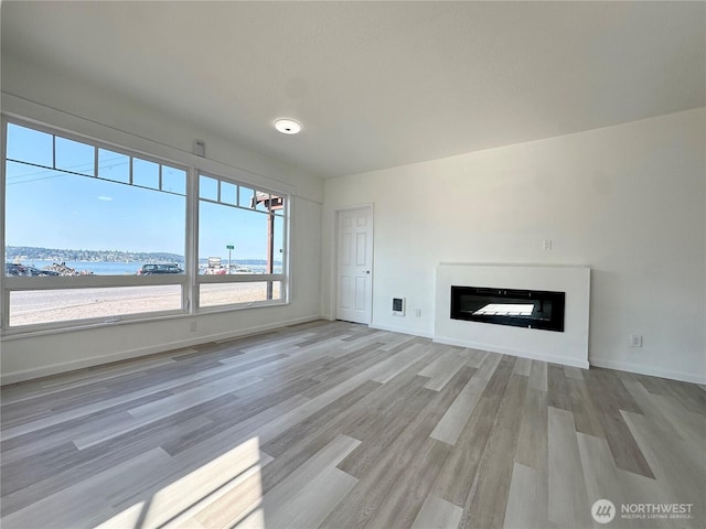 unfurnished living room with wood finished floors, a glass covered fireplace, and baseboards