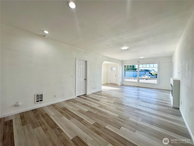 unfurnished living room featuring arched walkways, baseboards, visible vents, and light wood finished floors