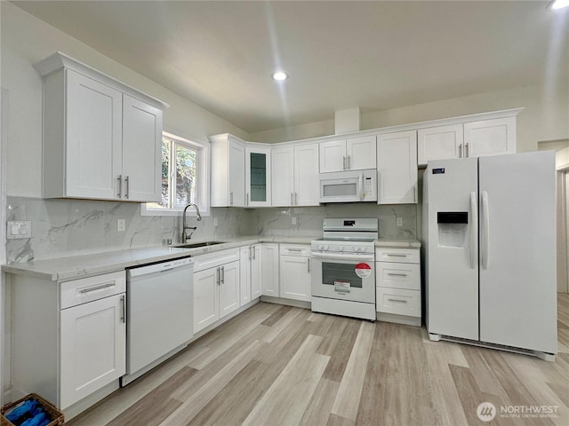 kitchen with white appliances, light wood finished floors, a sink, white cabinetry, and backsplash