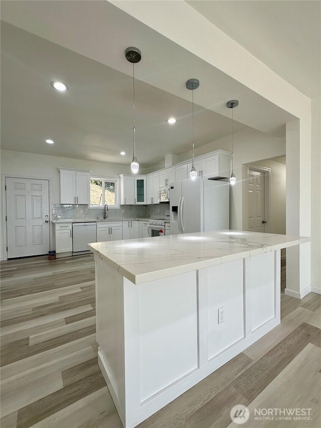 kitchen featuring white appliances, decorative backsplash, light wood-style floors, white cabinetry, and a sink