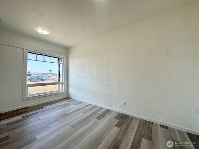 spare room featuring a textured wall, a textured ceiling, baseboards, and wood finished floors