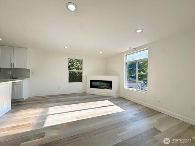 unfurnished living room featuring light wood-style floors, a glass covered fireplace, and recessed lighting