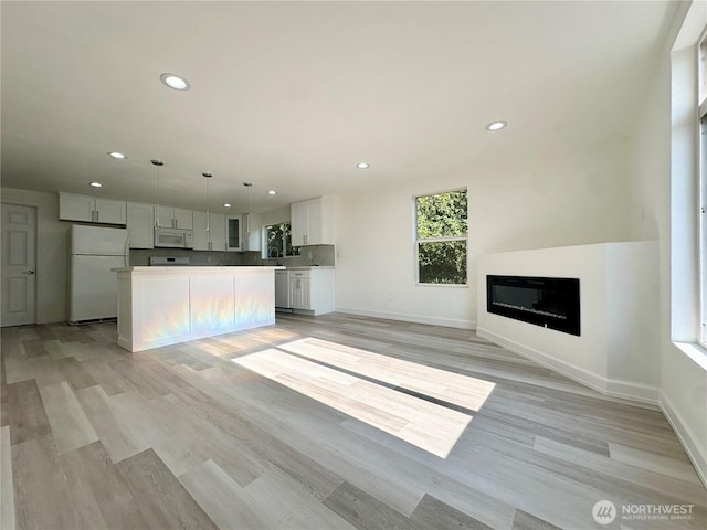 kitchen with light wood-style flooring, recessed lighting, white appliances, a kitchen island, and white cabinetry