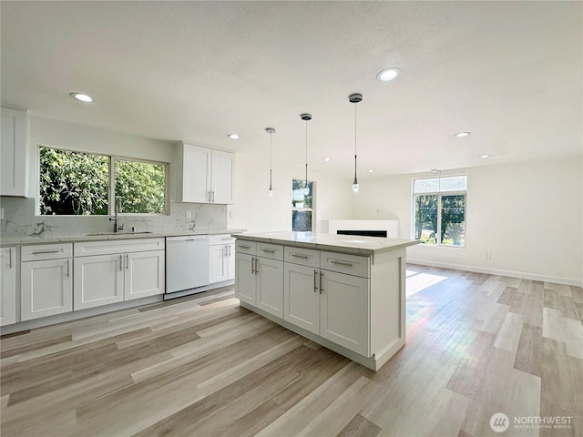 kitchen with a sink, white cabinets, a center island, dishwasher, and light wood finished floors