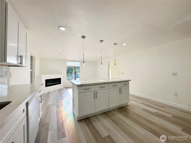 kitchen with light wood finished floors, a glass covered fireplace, dishwashing machine, light stone counters, and a textured ceiling