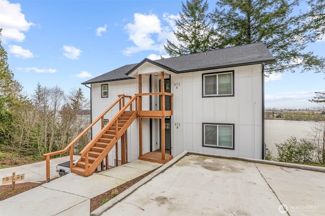 view of front of property with board and batten siding, roof with shingles, a patio, and a water view