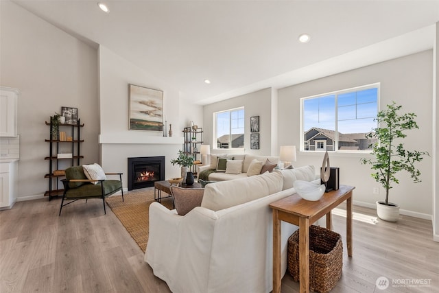 living area featuring a glass covered fireplace, light wood-style flooring, baseboards, and recessed lighting