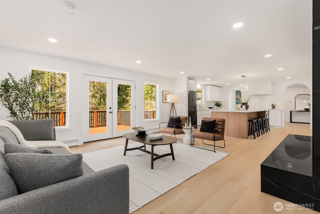 living area with arched walkways, recessed lighting, french doors, and light wood-style flooring