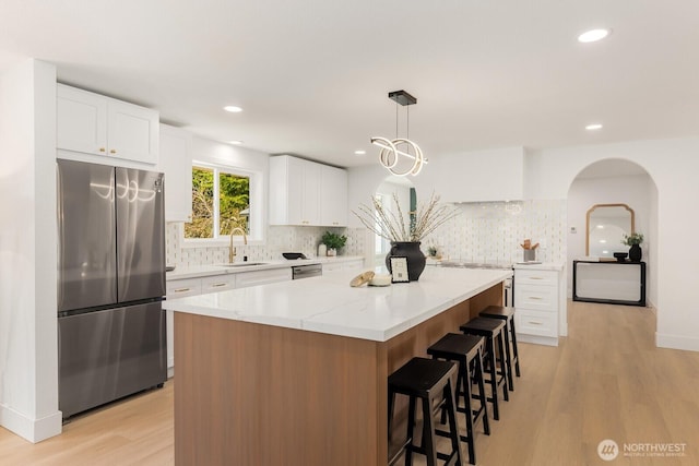 kitchen with a center island, light wood finished floors, a breakfast bar area, stainless steel appliances, and a sink