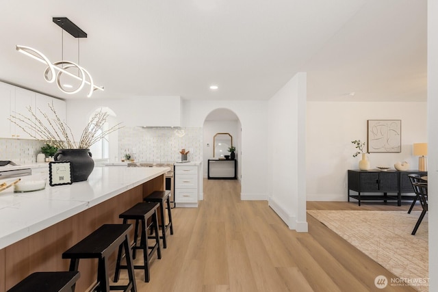 kitchen with arched walkways, a breakfast bar, white cabinetry, backsplash, and light wood finished floors