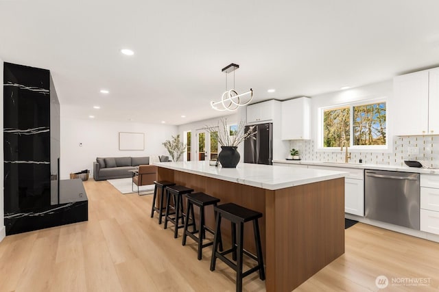 kitchen with refrigerator, a kitchen island, a sink, stainless steel dishwasher, and light wood finished floors