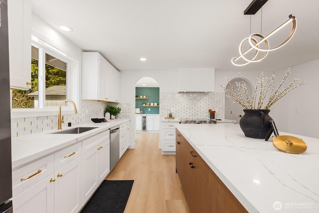 kitchen with light stone counters, a sink, white cabinets, light wood-type flooring, and dishwasher