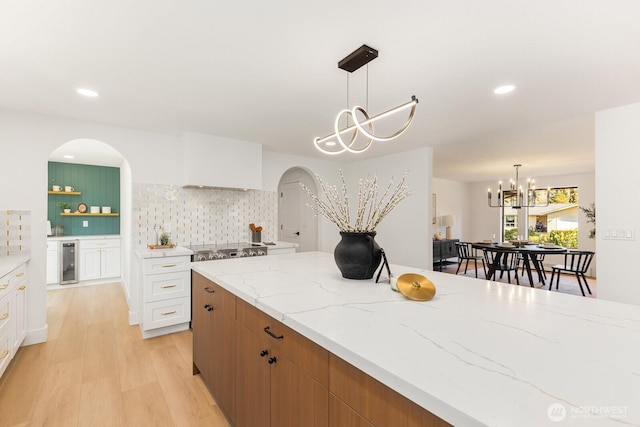 kitchen with light stone counters, tasteful backsplash, a chandelier, light wood-type flooring, and beverage cooler