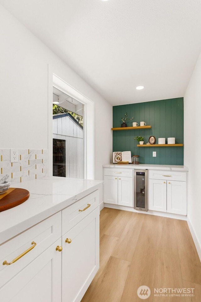 bar with beverage cooler, backsplash, light wood-style flooring, and baseboards