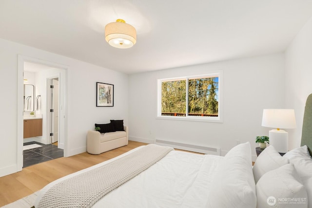 bedroom with ensuite bath, baseboards, baseboard heating, and wood finished floors