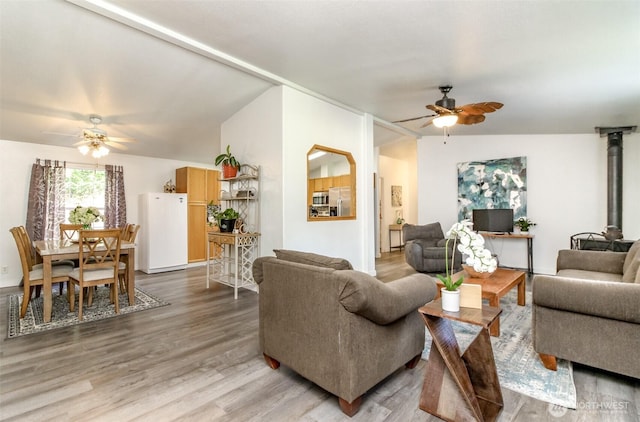 living room featuring light wood finished floors, ceiling fan, a wood stove, and lofted ceiling