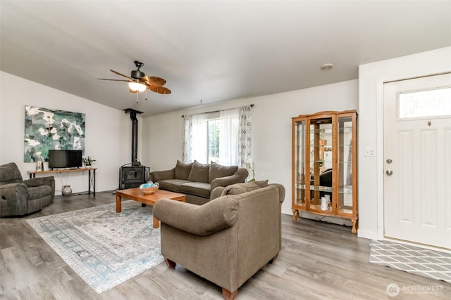 living area with a ceiling fan, lofted ceiling, a wood stove, and light wood-style flooring