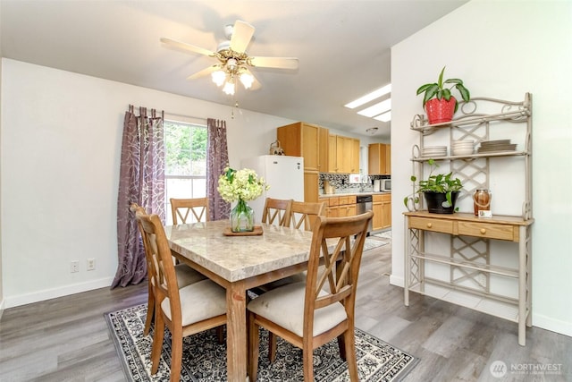 dining room featuring light wood-type flooring, baseboards, and a ceiling fan