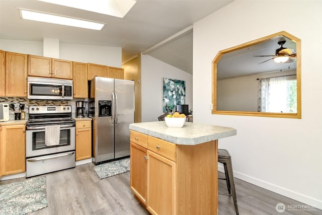 kitchen featuring a breakfast bar area, stainless steel appliances, light countertops, vaulted ceiling, and light wood-style floors