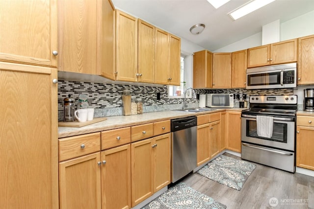 kitchen with light wood-type flooring, light countertops, lofted ceiling, stainless steel appliances, and a sink