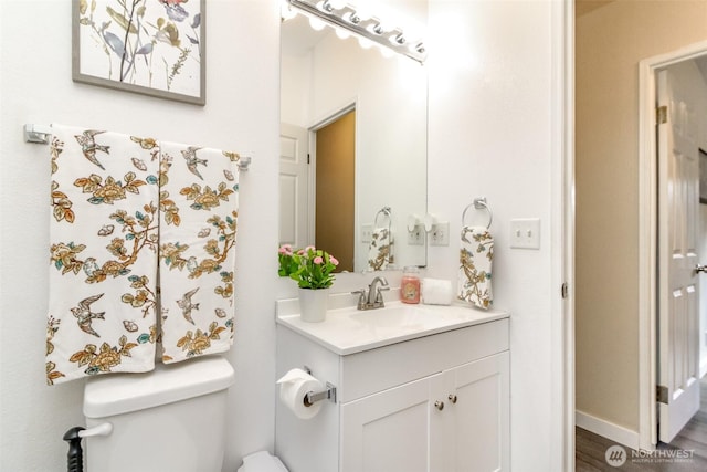 half bathroom featuring baseboards, toilet, and vanity