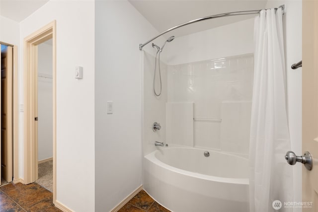 bathroom with stone finish floor, baseboards, and shower / bath combo with shower curtain