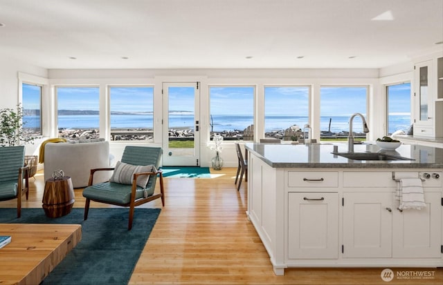 kitchen with dark stone countertops, white cabinets, light wood-type flooring, and a sink