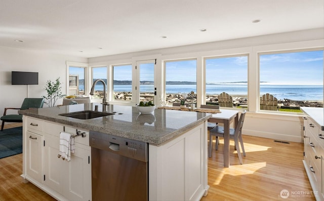 kitchen with stainless steel dishwasher, an island with sink, light wood-style floors, and a sink