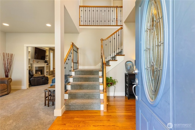 entryway with baseboards, stairway, wood finished floors, a lit fireplace, and recessed lighting