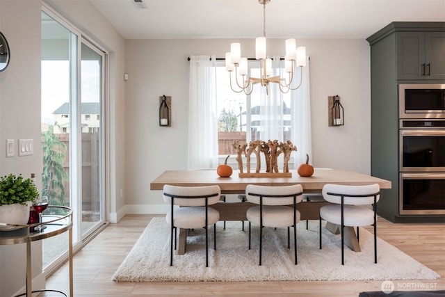 dining room featuring light wood-type flooring, a notable chandelier, and baseboards