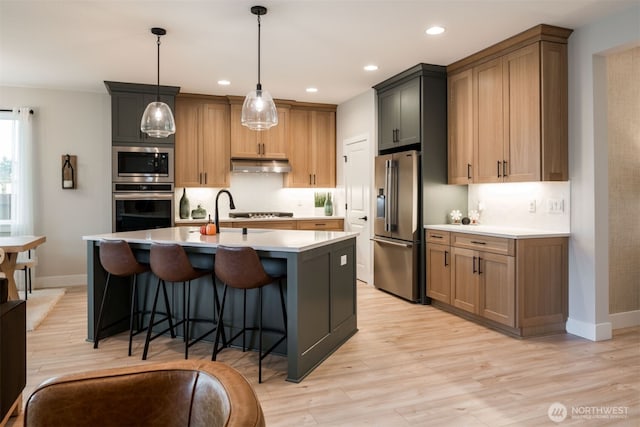 kitchen with under cabinet range hood, backsplash, stainless steel appliances, and light countertops