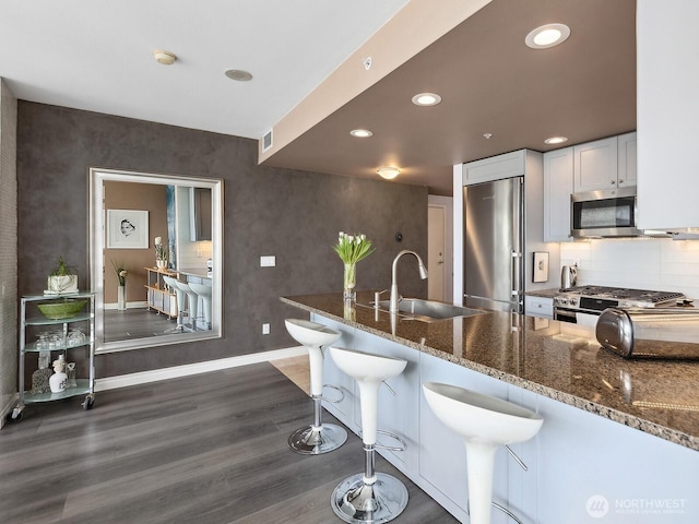 kitchen featuring dark stone counters, appliances with stainless steel finishes, dark wood-style floors, white cabinets, and a sink